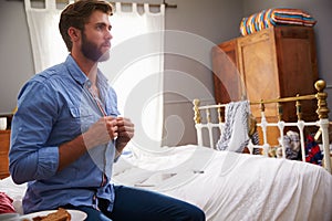 Man Sitting On Bed Getting Dressed In Morning