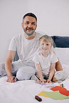 Man sitting on bedding near adorable son making fathers day greeting card