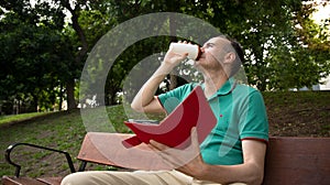 man sitting on a bench drinking coffee with an e-book in his hand