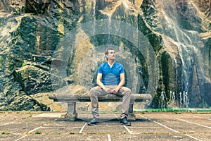 Man sitting on a stone bench and thinking with his back to a waterfall