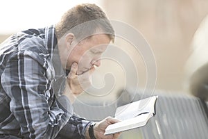 Man sitting on bench and reading bible
