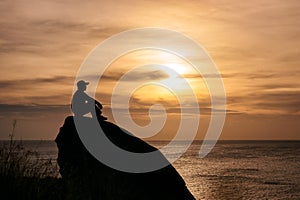 Man sitting on big rock with sightseeing of sunset in tropical sea