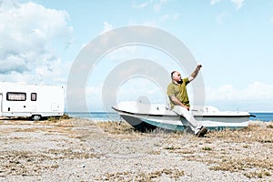 Man sitting in boat on the beach near his white camper van parked by the sea. Tourist season on the mediterranean sea.