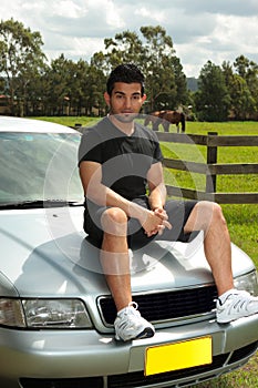 Man sitting on bonnet of silver car in countryside