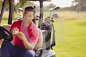 Man Sitting In Buggy Playing Round On Golf And Checking Score Card