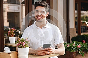 Man sitting in cafe outdoors while using mobile phone.