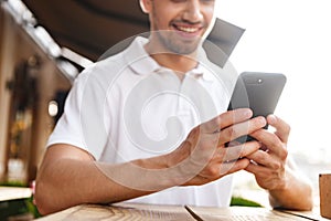 Man sitting in cafe outdoors while using mobile phone.