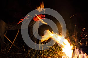 Man sitting on a camping chair warming his hands by the fire on a dark night