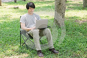 Man sitting on camping chair and working with laptop computer in the garden