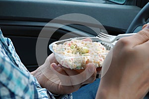 Man, sitting in a car, eats a salad with mayonnaise from plastic disposable dishes