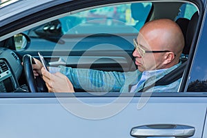 Man sitting in car with mobile phone in hand texting while driving