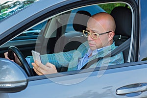 Man sitting in car with mobile phone in hand texting while driving