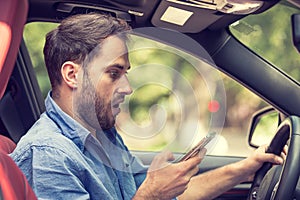 Man sitting in car with mobile phone in hand texting while driving