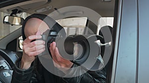 A man sitting in a car and taking a photo with a professional camera, a private detective or a paparazzi spy.