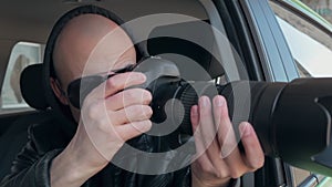A man sitting in a car and taking a photo with a professional camera, a private detective or a paparazzi spy.