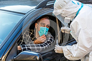 Man sitting in car, waiting for medical worker in PPE to perform drive-thru COVID-19 test