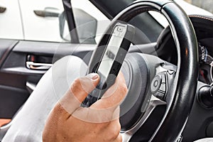 A man sitting in a car and writing a work message on a mobile phone. Open car door. Mobile phone with protective glass