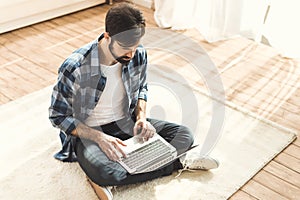 Man sitting on carpet and typing on laptop