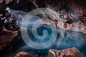 Man sitting in cave with blue geothermal pool