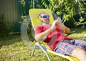 Man sitting in the chair with a mobile Phone in hands. Summer time. Shopping online.