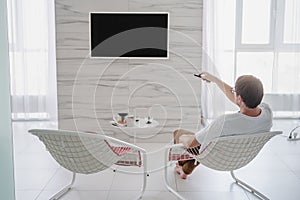 Man sitting in a chair watching tv holding remote control