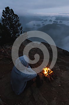 Man sitting on cliff with campfire above coastal view on bay in the evening