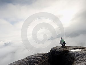 Man sitting on cliff enjoying mountains and clouds landscape