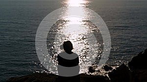 Man sitting on a cliff in front of the sun`s reflection