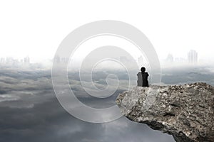 Man sitting on cliff with gray cloudy sky cityscape background