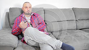 Man sitting on comfortable sofa in living room alone, holding remote control, switching channels, watching TV