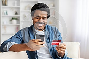 Man Sitting on Couch Holding Smart Phone and Credit Card