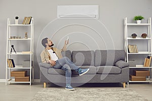 Man sitting on couch at home and adjusting air conditioner mode with remote control