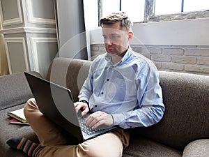 A man is sitting on the couch at home and typing on a laptop.