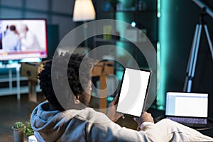 Man sitting on couch, reading eBook from tablet in apartment using mockup tablet