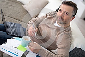 man sitting on couch studying using laptop and headset