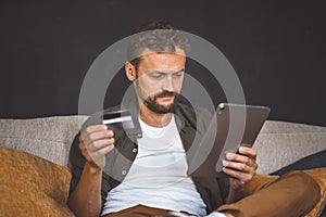 Man Sitting on Couch With Tablet and Credit Card