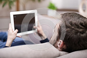 A man sitting on the couch uses a tablet PC. Back view.