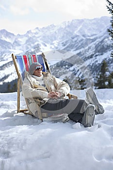 Man Sitting On Deckchair In Snowy Mountains