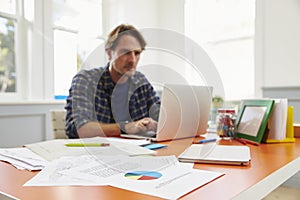 Man Sitting At Desk Working At Laptop In Home Office