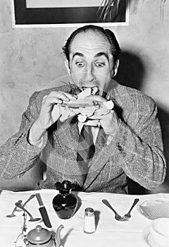 Man sitting at a dining table and trying to eat a sandwich