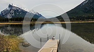 Man sitting on dock in front of lake and mountains