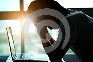 A man sitting down, his face unsettled. At the computer desk He has headaches and stress. Cause of hard work and insufficient rest