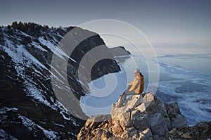 Man Sitting on Edge of Cliff and Looking on Frozen Lake Baikal in Winter. Olkhon Island, Russia