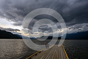 Man sitting on the edge of a wooden dock on Harrison Lake and watching the coming storm