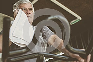 Man sitting on exercise machine. Man wipes his face with