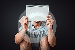 Man sitting on the floor with black color background and holding blank notebook, copy space, homeless concept