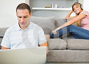 Man sitting on floor with laptop with woman listening to music o