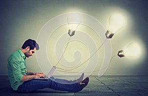 man sitting on floor using a laptop with many light bulbs plugged in it