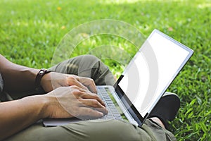 The man sitting on the floor of the yard, hand typing to working laptop mockup white screen.outdoor