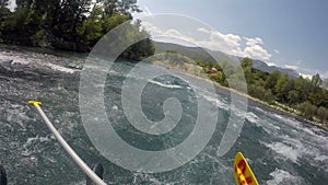 A man is sitting on the front of the boat with his legs dangling down making a rafting trip on a mountain river